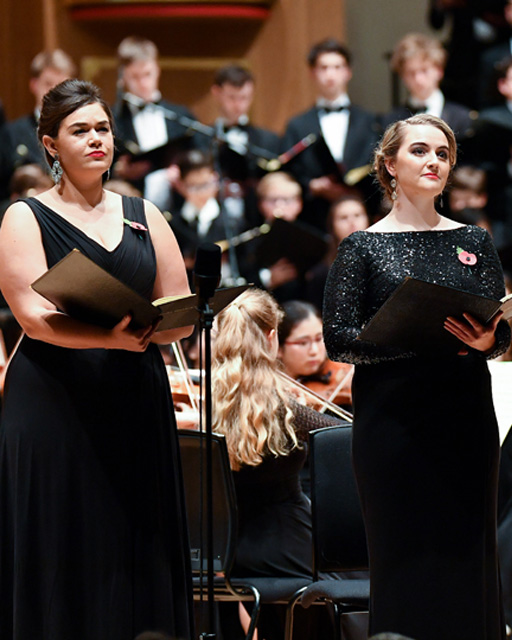 Two RCM singers in performance with an orchestra and choir.